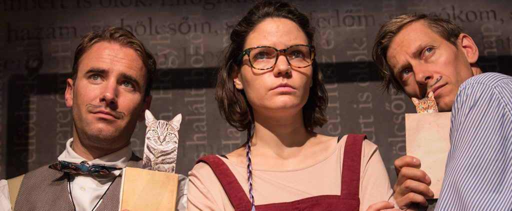 Three actors from Kolibri Szinhaz's production "withoutfather withoutmother". Two men hold books with drawen on moustaches and a woman wears glasses. 