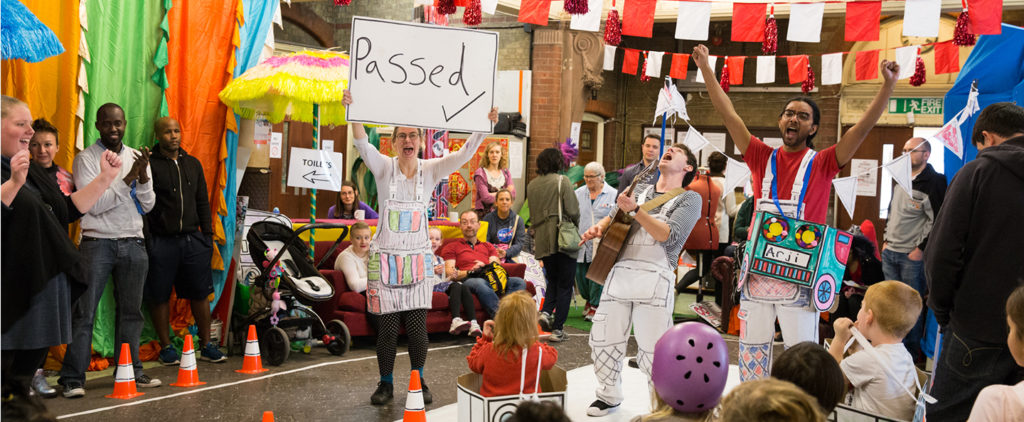 Three performers dressed in handmade costumes celebrating in a room full of children.